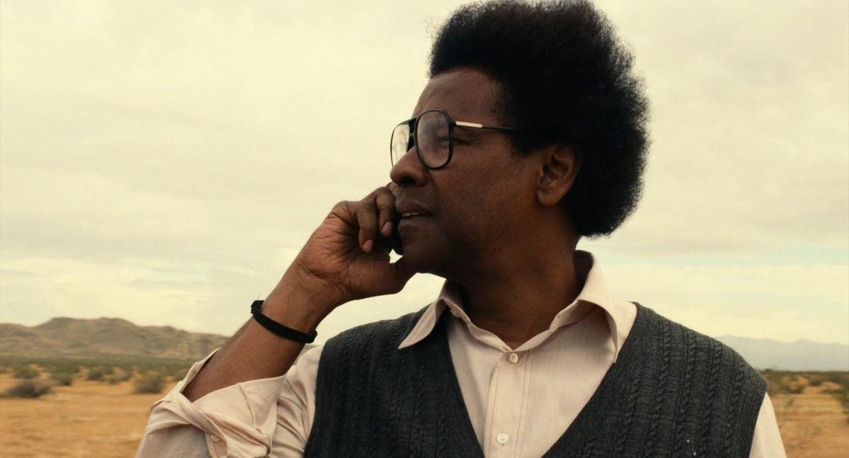 Denzel Washington tiene il telefono all'orecchio destro mentre si trova nel deserto in Roman J. Israel, Esq.  Ha i capelli arruffati e indossa grandi occhiali e un gilet.