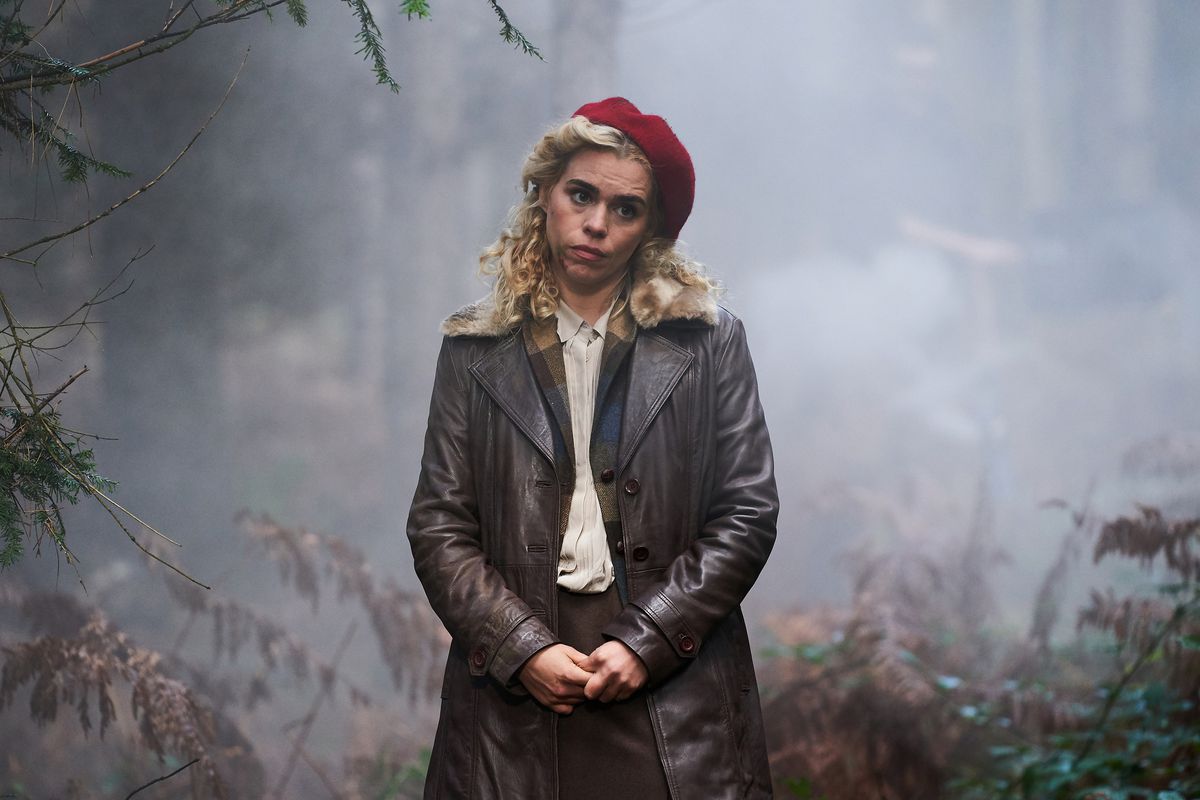 Billie Piper inclina la testa mentre indossa un berretto rosso e un cappotto nero in una specie di area boschiva in I Hate Suzie.