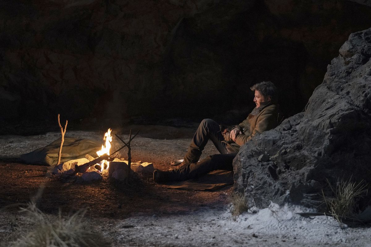 Joel (Pedro Pascal) seduto e appoggiato a un muro di roccia e guardando un fuoco