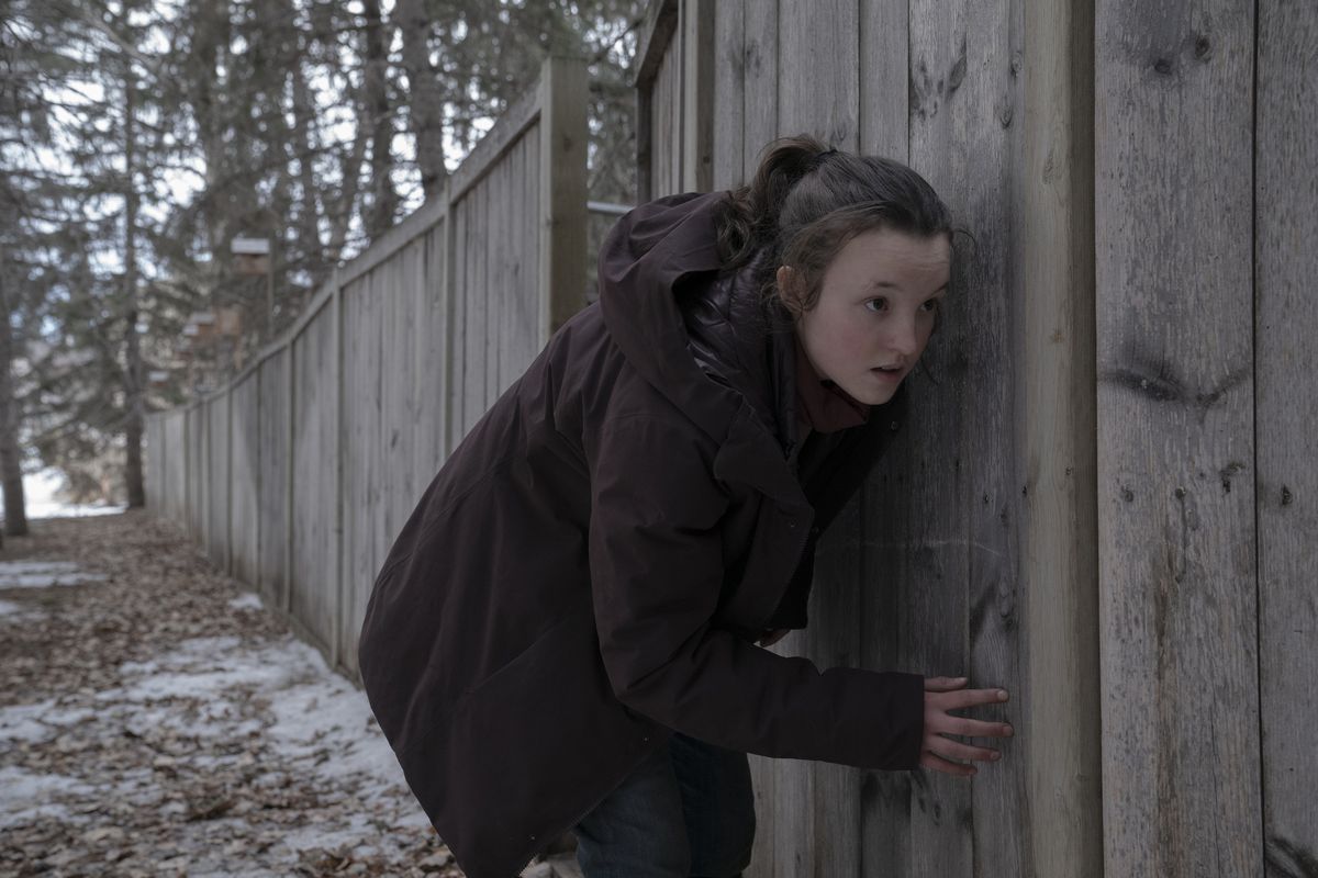 Ellie si accovaccia e si schiaccia contro una staccionata di legno in inverno in una scena di The Last of Us della HBO