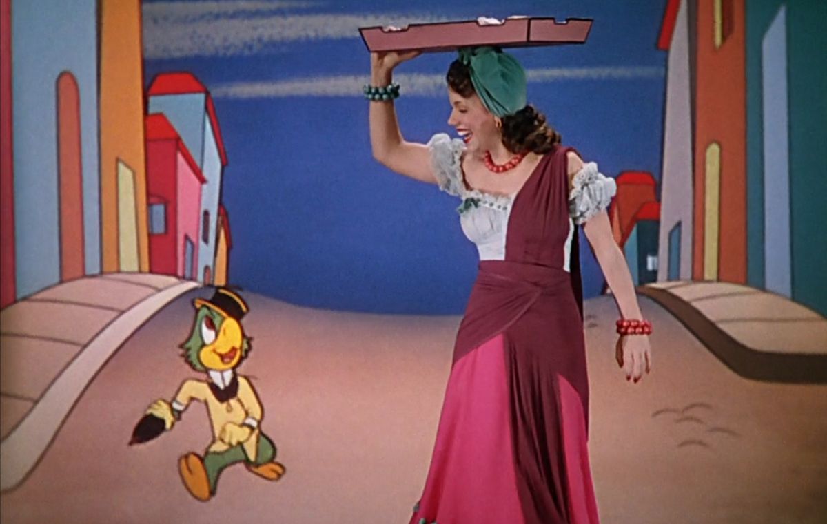 Il pappagallo dei cartoni animati José Carioca, con cappello a tre punte e giacca gialla, cammina accanto alla cantante live-action Aurora Miranda in una strada dei cartoni animati in Brasile nel cortometraggio Disney 