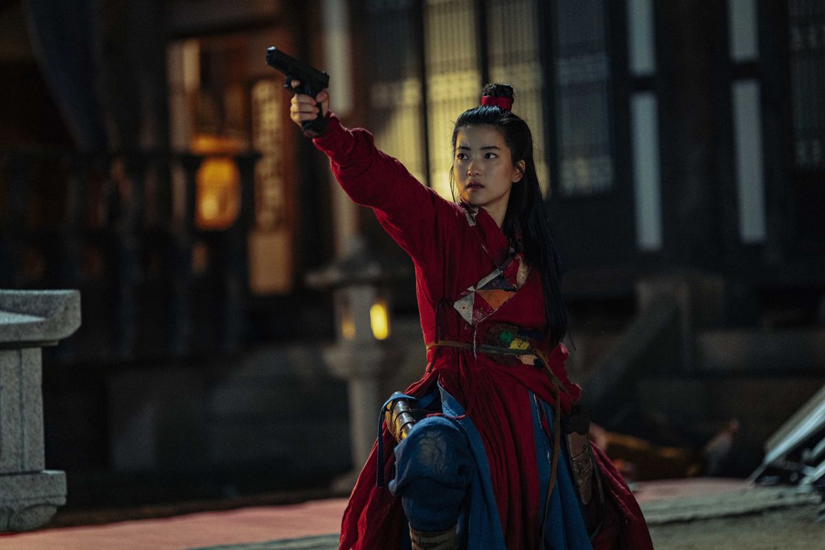 Una donna (Kim Tae-ri) con i capelli raccolti in una crocchia vestita con un kimono rosso e blu punta una pistola fuori campo mentre è inginocchiata in mezzo a un cortile.