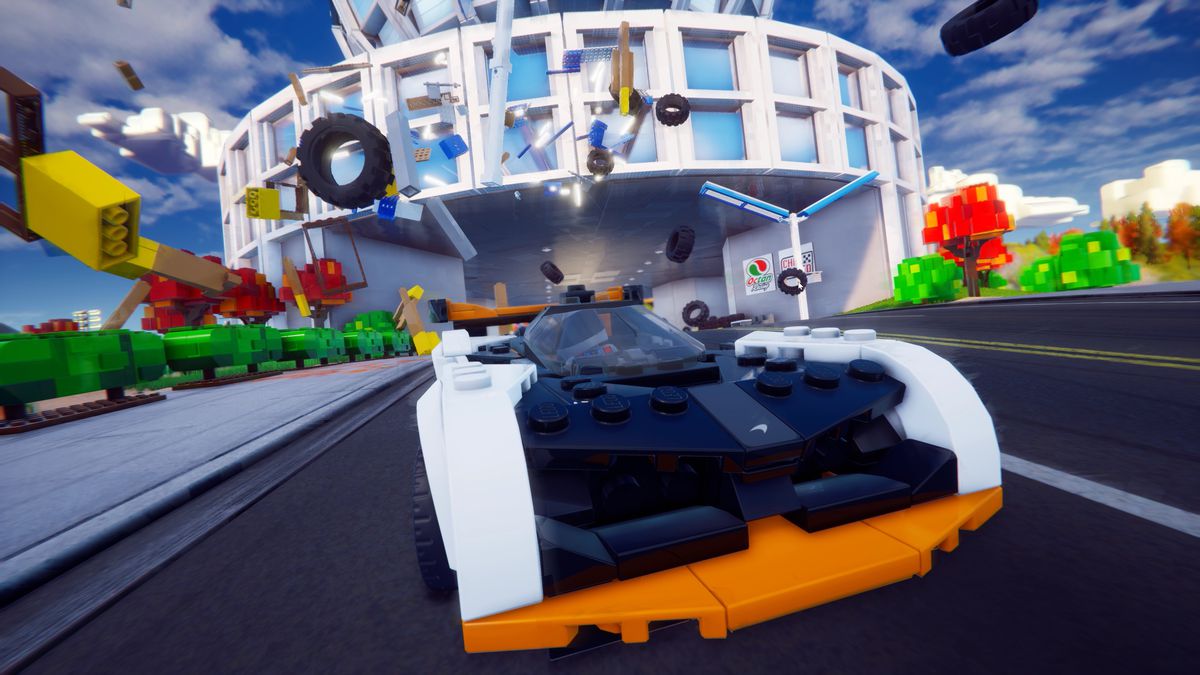 Uno screenshot di Lego 2K Drive, che mostra un'auto da corsa che esplode attraverso una costruzione Lego e spruzza mattoni e pneumatici ovunque