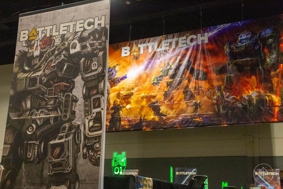Uno standee di un mech Atlas, il suo teschio corazzato che domina l'immagine.  Sullo sfondo, grafica completa per il cofanetto BattleTech.