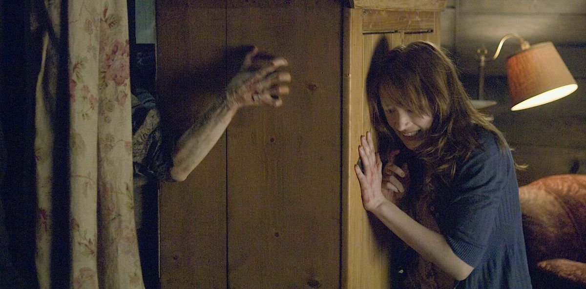 Dana (Kristen Connolly) spinge un alto armadio di legno contro una finestra rotta mentre gli zombi cercano di farsi strada nella sua capanna rustica in The Cabin in the Woods del 2011