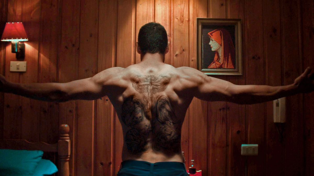 Marko Zaror, a torso nudo, allunga le braccia mentre vediamo la sua schiena piena di tatuaggi, in Redeemer.