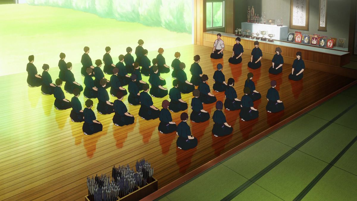 Un gruppo di studenti di Kyudo seduti sull'attenti in una sala di tiro con l'arco di fronte a un gruppo di cinque istruttori.