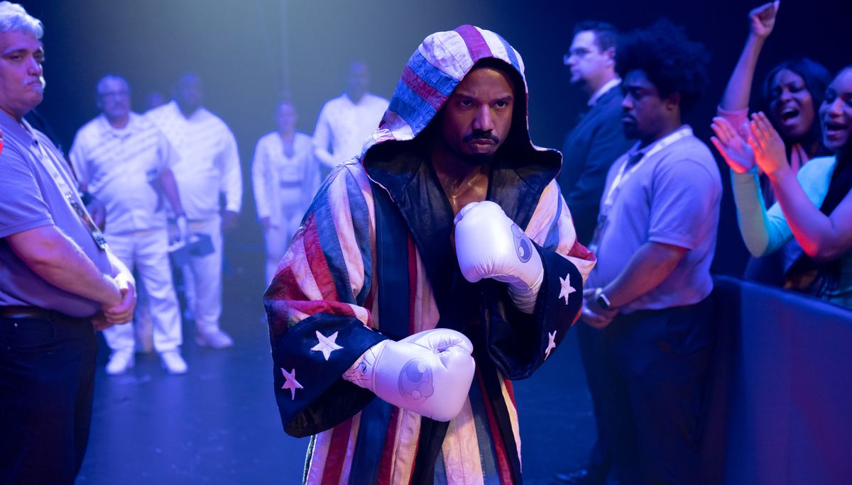 Adonis Creed (Michael B. Jordan) si prepara a salire su un ring di pugilato, con guanti bianchi e una veste con cappuccio a tema bandiera americana rossa, bianca e blu in Creed III