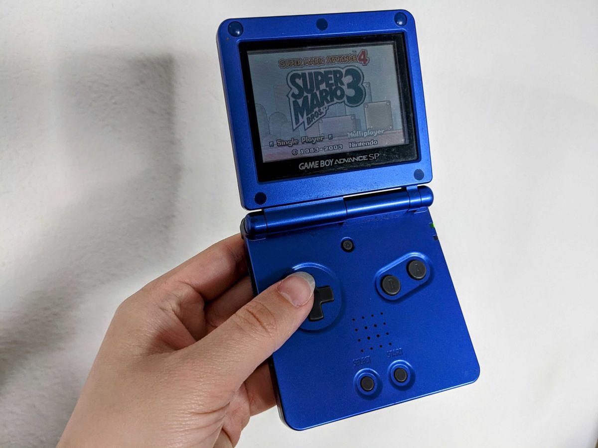 Una mano che tiene un Game Boy Advance SP viola con Super Mario Bros. 3 appena visibile sullo schermo.