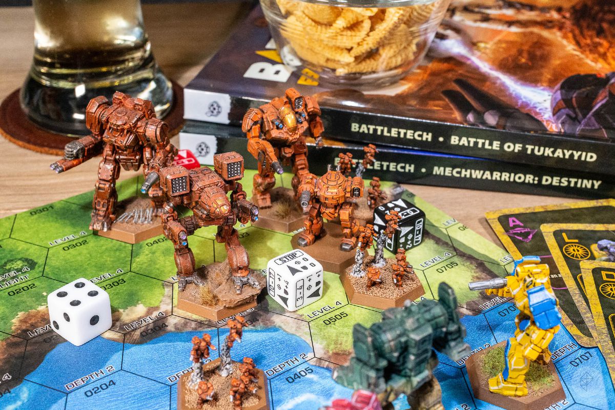Miniature Battletech impegnate in combattimento.  Birra e arachidi per aromatizzare.