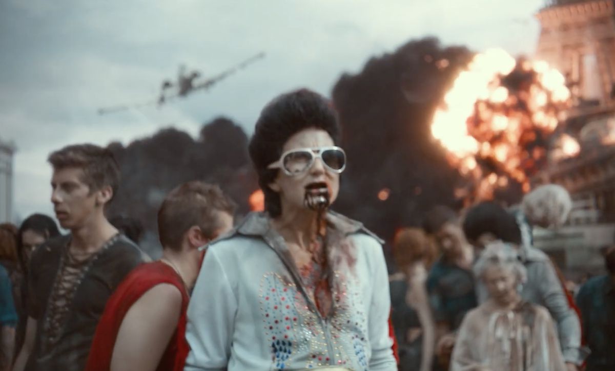 Uno zombi imitatore di Elvis si aggira per Las Vegas con altri zombi mentre alle loro spalle avviene un'esplosione in Army of the Dead.