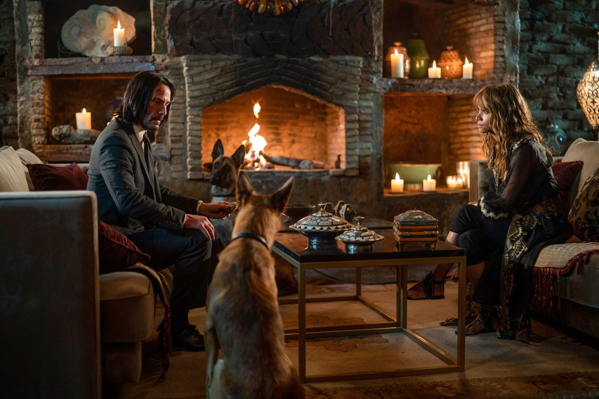 John Wick siede in un atrio elaborato accanto a un caminetto di fronte a Sofia e tra i suoi cani in John Wick: Capitolo 3