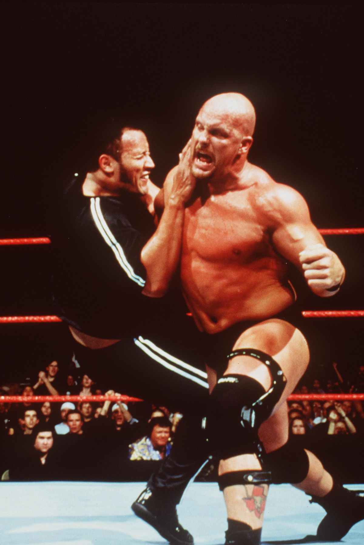Stone Cold Steve Austin sbatte The Rock sul pad mentre i fan esultano fuori dal ring a WWF Smackdown