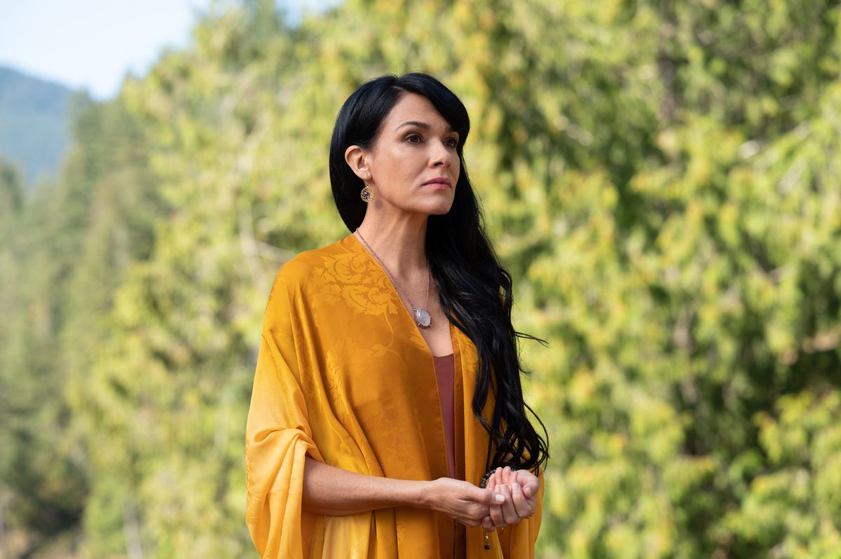 L'adulta Lottie si trova in una pittoresca ambientazione boscosa in uno scialle giallo fluente nella premiere della seconda stagione di Yellowjackets.