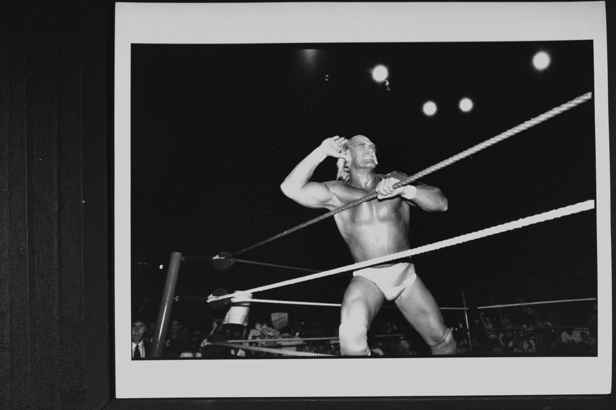 Una foto in bianco e nero mostra Hulk Hogan in un ring di wrestling nel fiore degli anni, che invita la folla a fare rumore.