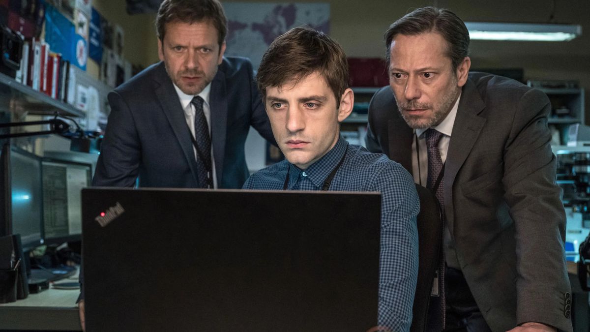 Tre uomini - due in giacca e cravatta, uno in camicia con colletto - si rannicchiano attorno a un laptop aperto e lo fissano in The Bureau.
