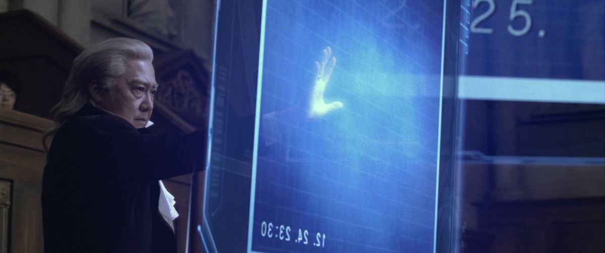 Un procuratore allunga la mano per toccare un gigantesco schermo olografico nell'adattamento live action di Ace Attorney.