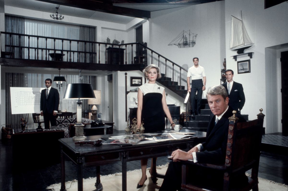 Greg Morris, Barbara Bain, Peter Lupus, Peter Graves, Martin Landau sono disposti attorno a un tavolo e delle scale in una foto del cast della serie TV originale Mission: Impossible.