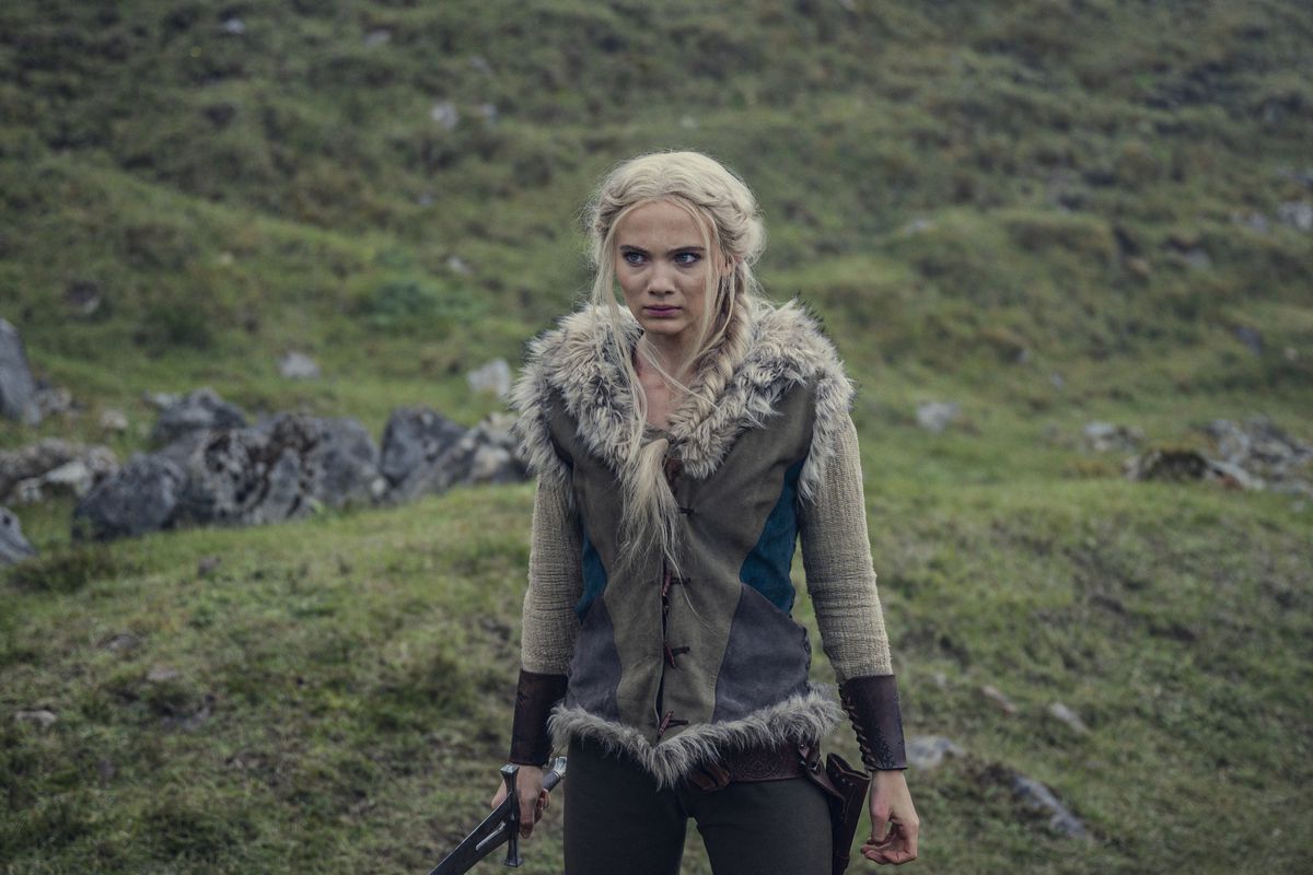 Freya Allen nei panni di Ciri nella terza stagione di The Witcher di Netflix è in piedi di fronte alla telecamera su una collina erbosa con una spada in mano