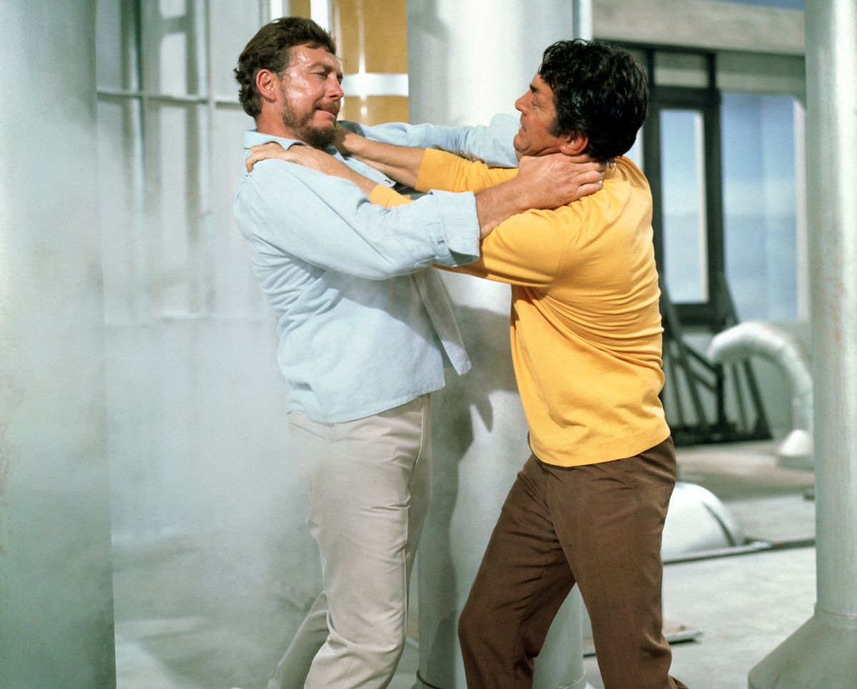 Matt Helm con un maglione giallo soffoca un ragazzo barbuto in pantaloni cachi su un'astronave in The Ambushers