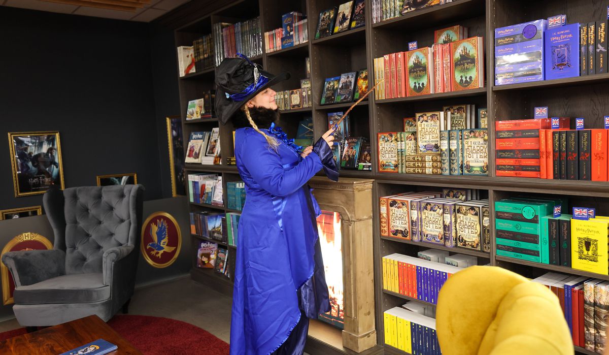 Un visitatore con una veste viola, con in mano una bacchetta magica, guarda una parete di libri e merchandising di Harry Potter all'inaugurazione di The Wizard World Shop - di Thalia ad Amburgo.