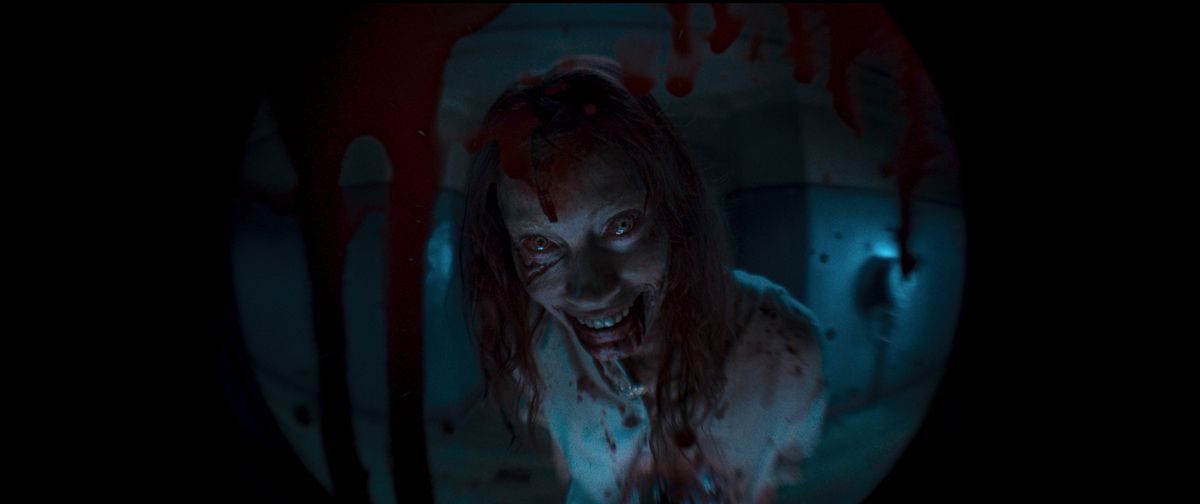 la Deadite Ellie fa un sorriso mostruoso dall'altra parte di uno spioncino macchiato di sangue in Evil Dead Rise