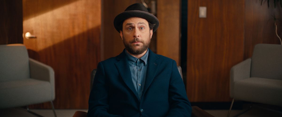 Charlie Day sembra sorpreso mentre indossa un abito e un cappello mentre è seduto su una sedia in un ufficio in Fool's Paradise.