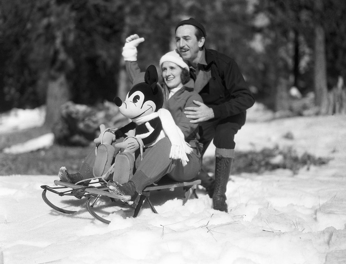 In un ritratto in bianco e nero non datato, Walk Disney si accovaccia dietro sua moglie Lillian e una bambola di Topolino, entrambi seduti su una vecchia slitta di legno con guide di metallo, all'aperto nella neve