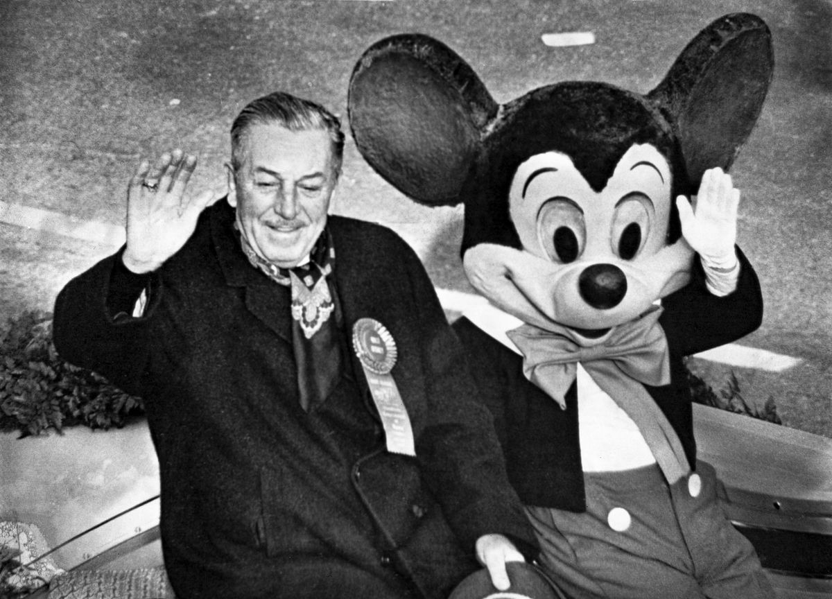 Una foto d'archivio di Walt Disney seduto accanto a un attore in costume nei panni di Topolino nel 1966 nei panni del Gran Maresciallo della Rose Parade, con entrambi che salutano il pubblico