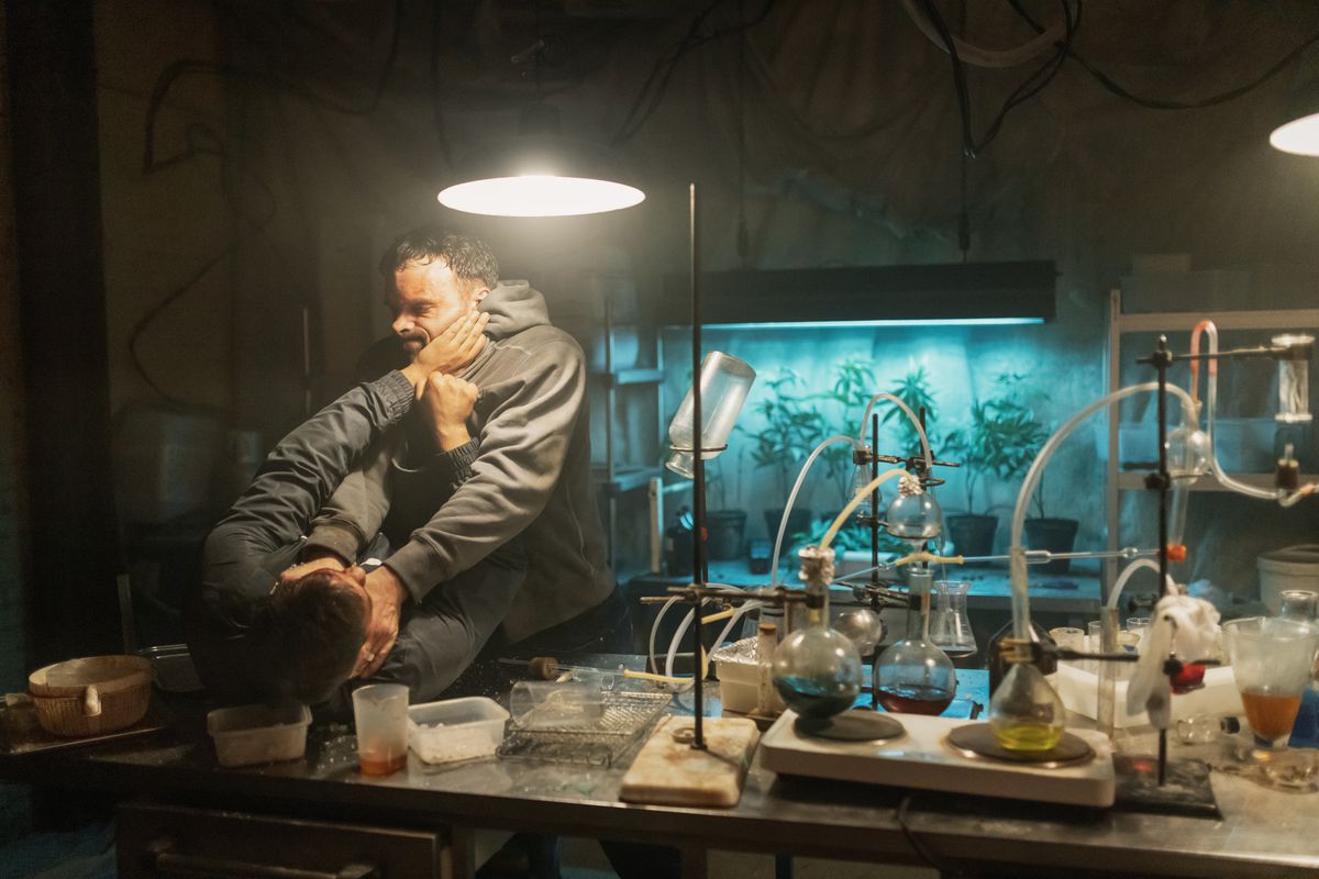 Alban Lenoir spinge un uomo in un tavolo pieno di apparecchiature chimiche in AKA.