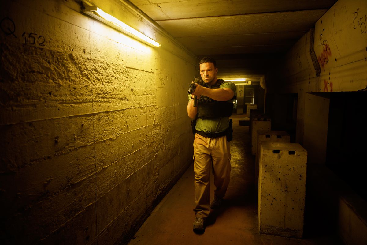 Alban Lenoir cammina attraverso un lungo corridoio mentre impugna un fucile d'assalto in AKA.