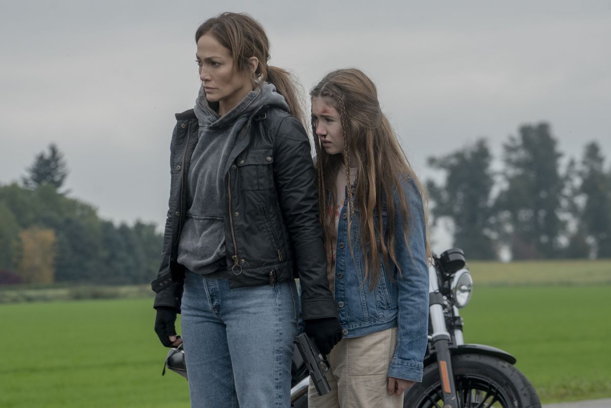 Jennifer Lopez, con indosso una giacca di pelle, sta protettivamente davanti a Lucy Paez, davanti a una motocicletta, in The Mother.