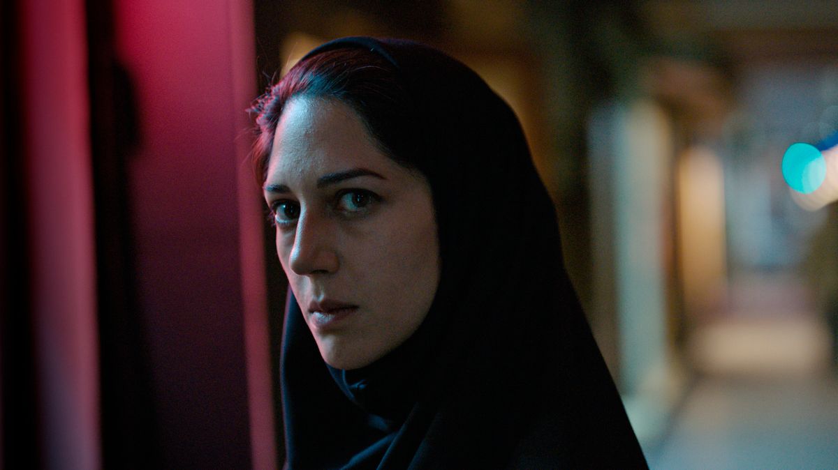 Arezoo Rahimi (Zahra Amir Ebrahimi) si trova nel mezzo di un corridoio buio con la luce riflessa sul lato del suo viso, i suoi capelli scuri parzialmente oscurati da un velo in Holy Spider.