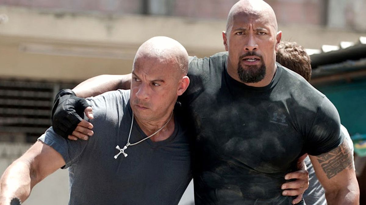 Dom (Vin Diesel) e Hobbs (Dwayne Johnson) si sostengono a vicenda con le braccia intorno alla vita l'uno dell'altro in Fast Five.  Il crocifisso di Dom, attualmente non consegnato a un membro della sua famiglia per custodia, pende ben visibile intorno al suo collo.