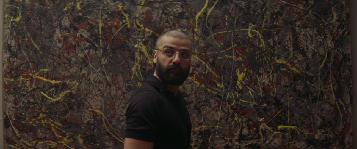 Oscar Isaac, capelli arruffati, occhiali e barba folta, è in piedi davanti a un muro dipinto (alla Jackson Pollack) in Ex Machina.