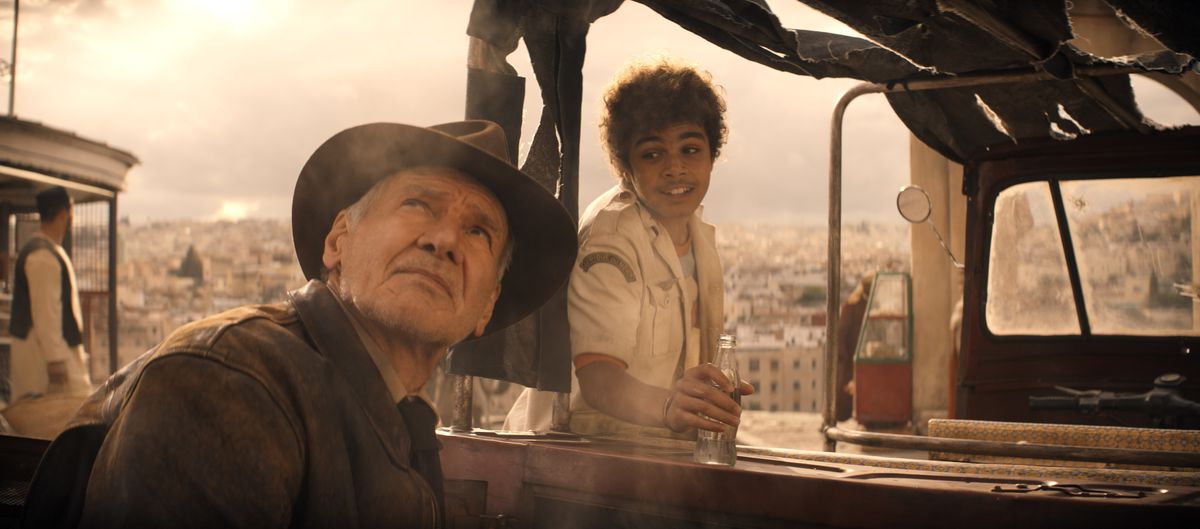 Indiana Jones (Harrison Ford) alza lo sguardo verso un cielo grigio coperto mentre un adolescente sorridente (Ethann Isidore) cerca di parlargli mentre si prepara a fare un giro sul suo camion in Indiana Jones e il quadrante del destino