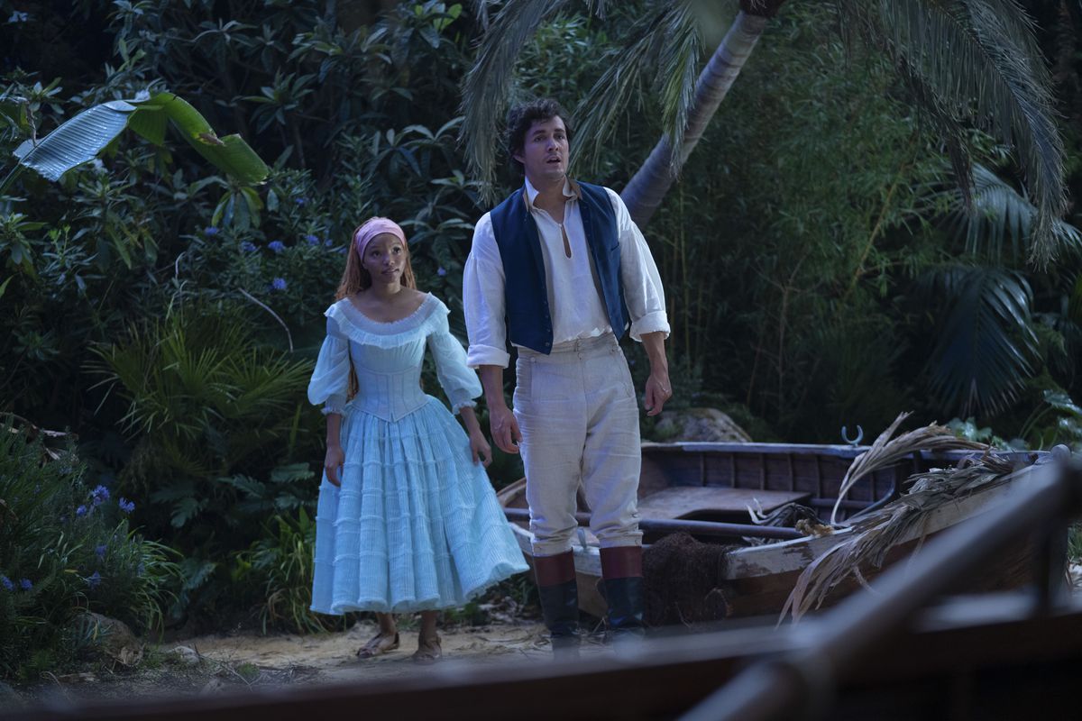 Eric e Ariel nel live-action La Sirenetta stanno su una spiaggia.  Ariel indossa un abito azzurro, mentre Eric indossa una camicia bianca con gilet blu e pantaloni kaki.