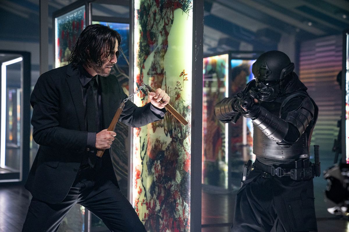 Keanu Reeves nei panni di John Wick che tiene num-chuk dietro un pannello di vetro che si prepara a tendere un'imboscata a un soldato in armatura nera da samurai in John Wick: Capitolo 4.