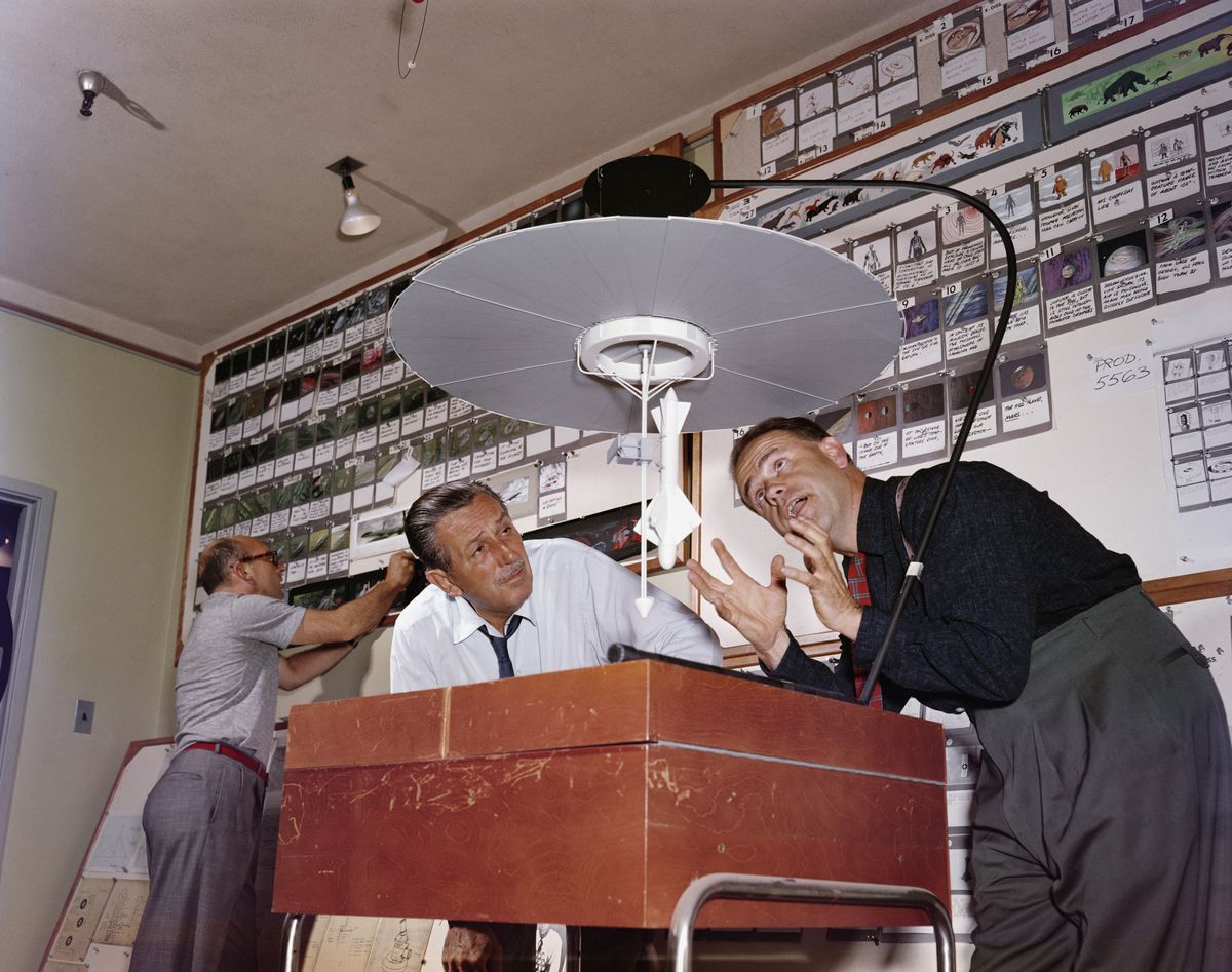 Walt Disney, a sinistra, in piedi accanto all'animatore Ward Kimball, con entrambi gli uomini chini su un lightbox sotto un'ampia lampada rotonda, davanti a un muro coperto di storyboard per una serie degli anni '50 chiamata Tomorrowland