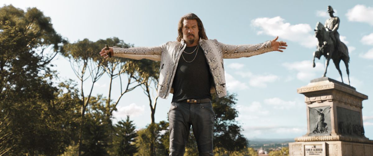 Dante (Jason Momoa), in una giacca di pelle di serpente tipicamente metrosessuale e pantaloni in vinile, allarga le braccia ai lati in un gesto drammatico in Fast X