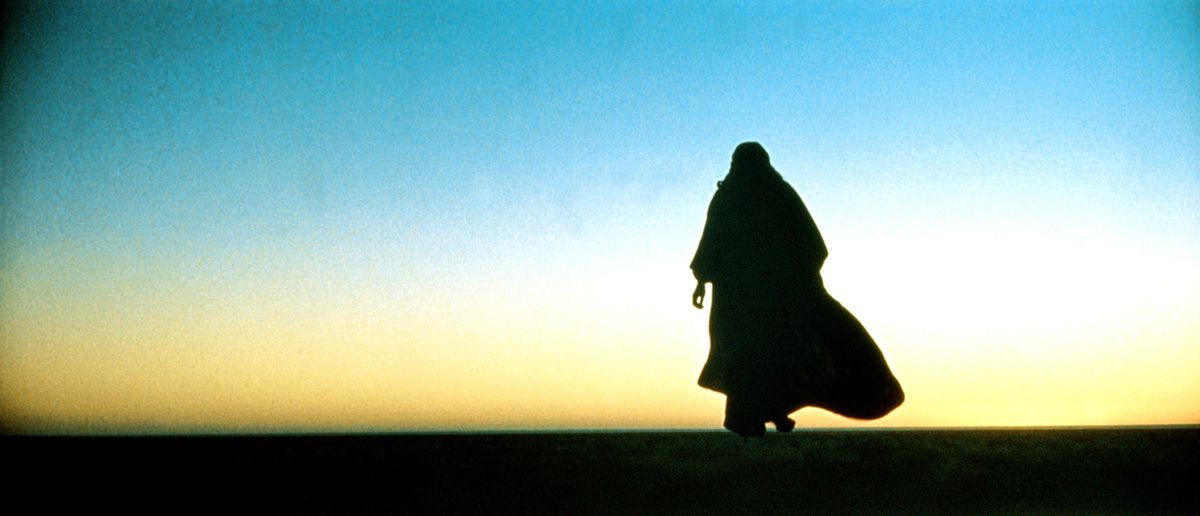 Un uomo nel tradizionale abito beduino si staglia contro un cielo al tramonto nel deserto