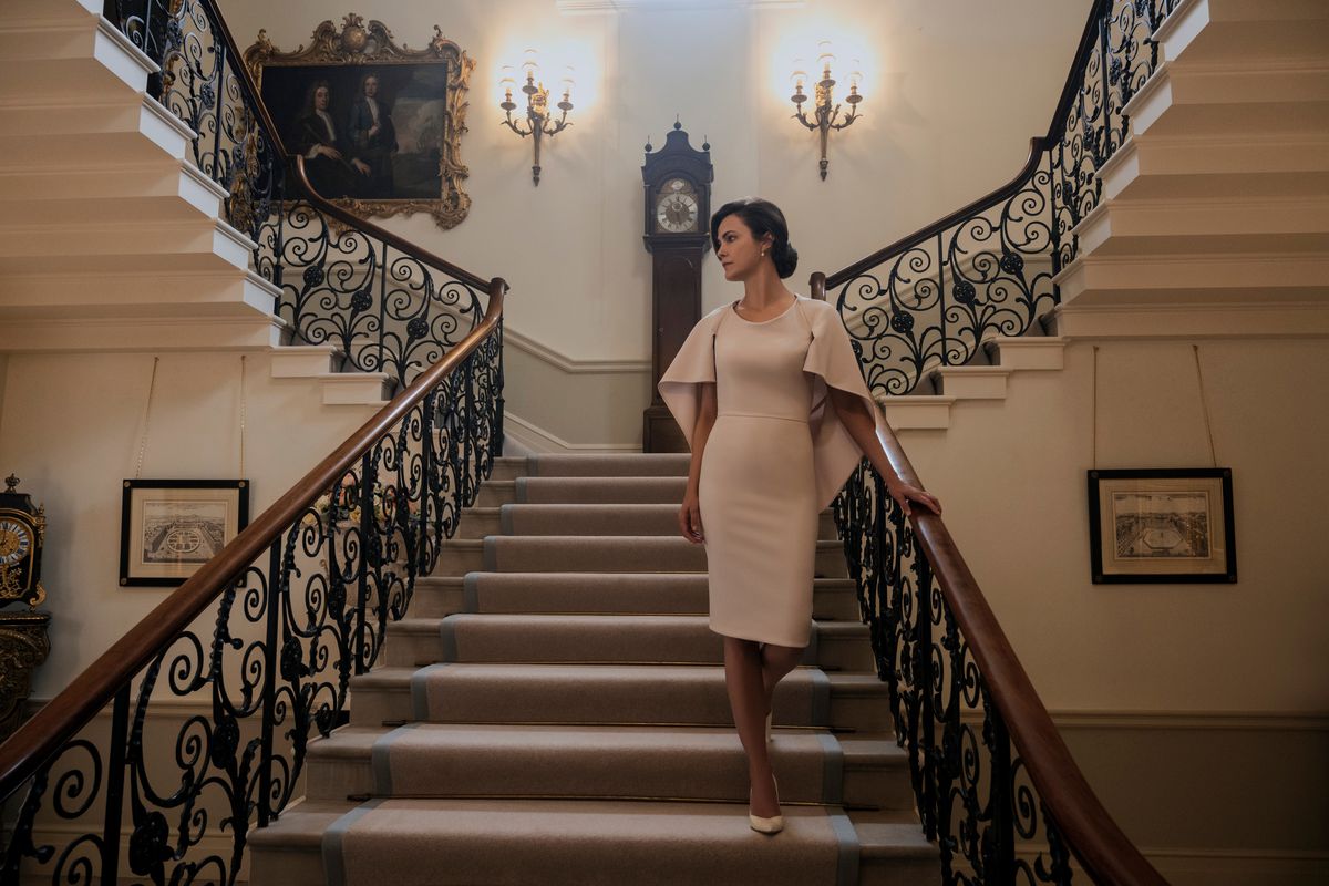 Keri Russell scende una scala stravagante mentre indossa un elegante abito beige in The Diplomat.