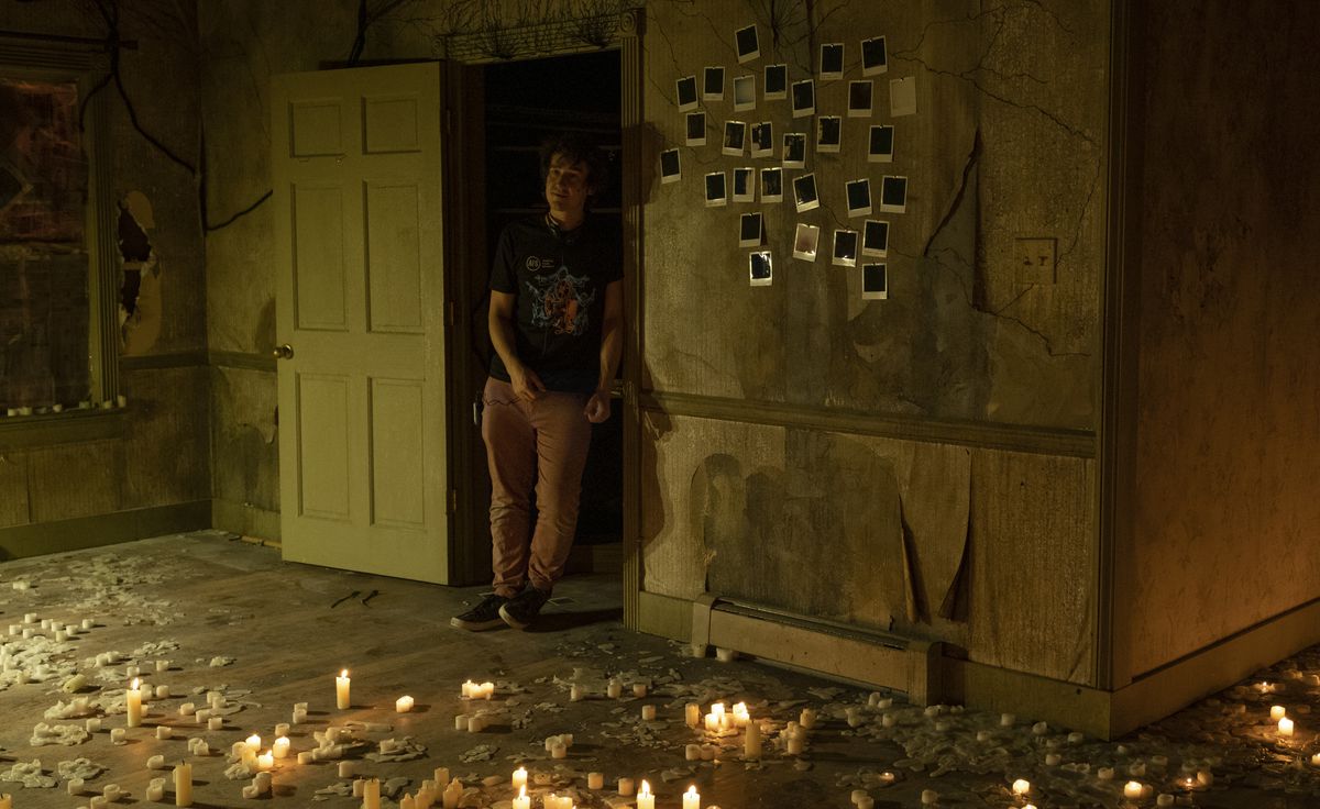Rob Savage in piedi in una casa fatiscente con polaroid sul muro illuminato da candele, ovvero il set di The Boogeyman