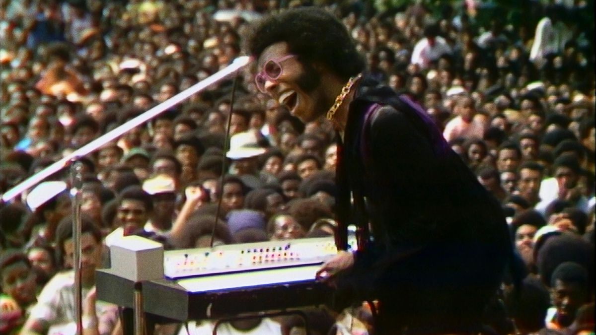 Sly Stone in performance con una folla enorme in sottofondo in Summer of Soul