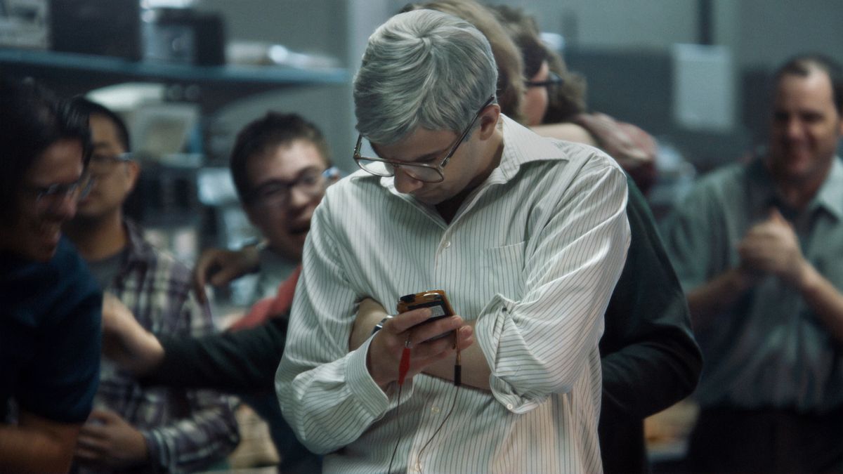 Jay Baruchel nei panni di un uomo con i capelli grigi e gli occhiali (Mike Lazaridis) che tiene in mano un prototipo di dispositivo BlackBerry in BlackBerry.