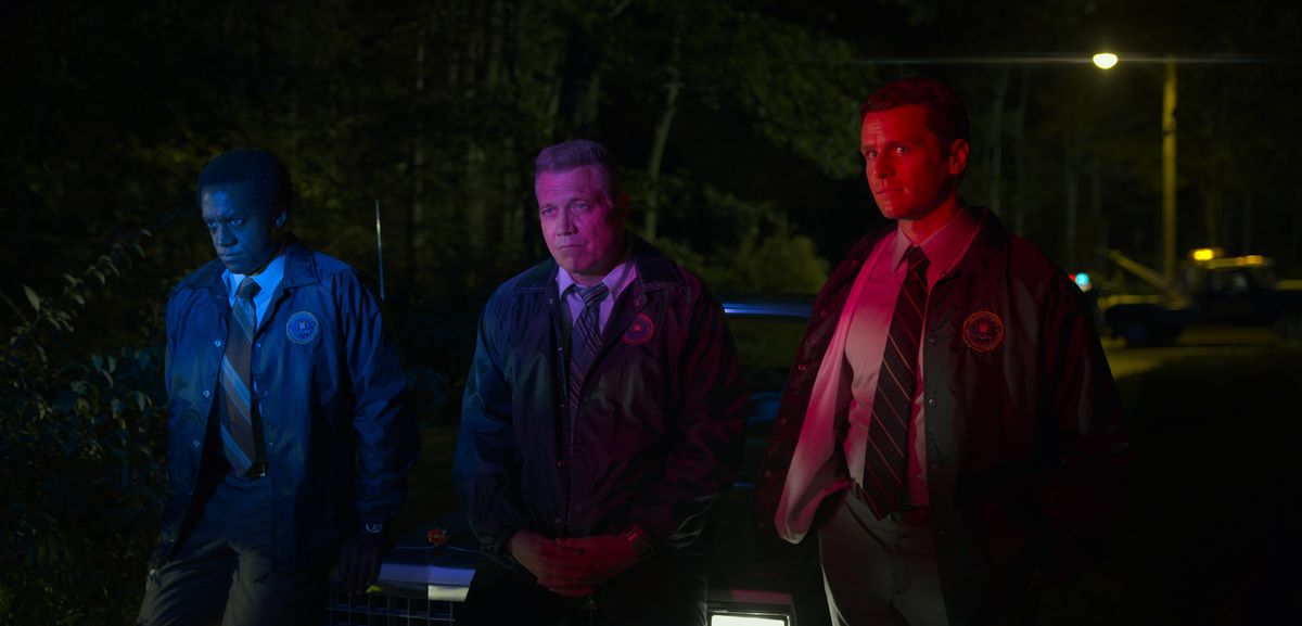 Albert Jones, Holt McCallany, Jonathan Groff appoggiati al cofano di un'auto illuminati dalle sirene della polizia nell'episodio cinque della stagione 2 di Mindhunter.