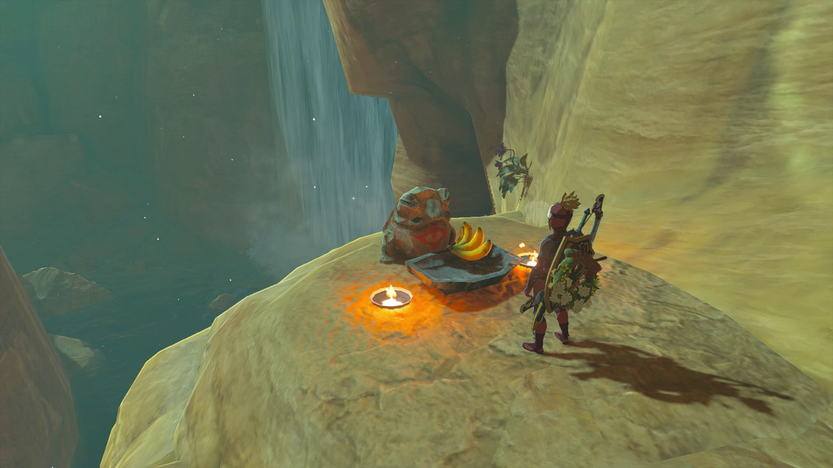 Link si trova di fronte a una rana con sopra il simbolo del clan Yiga in Tears of the Kingdom.  Ci sono due torce vicino alla rana con una banana offerta davanti.