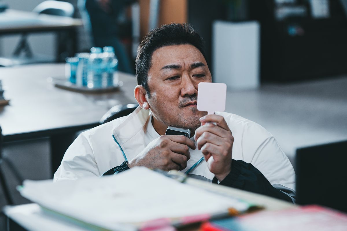 Ma Dong-seok tiene in mano uno specchio portatile mentre si fa la barba alla scrivania in The Roundup: No Way Out.