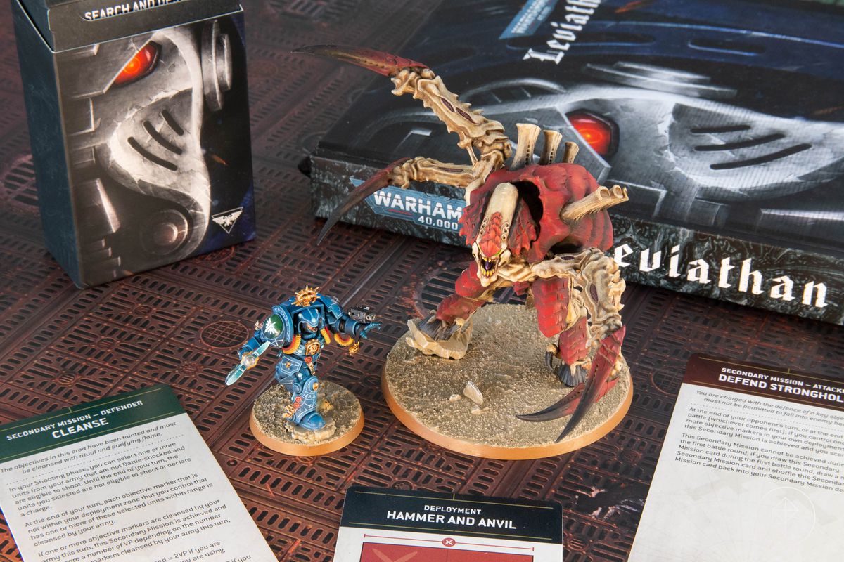 Due miniature pro-dipinte di Warhammer 40.000: Leviatano, un regolamento con copertina rigida e un assortimento di carte missione.